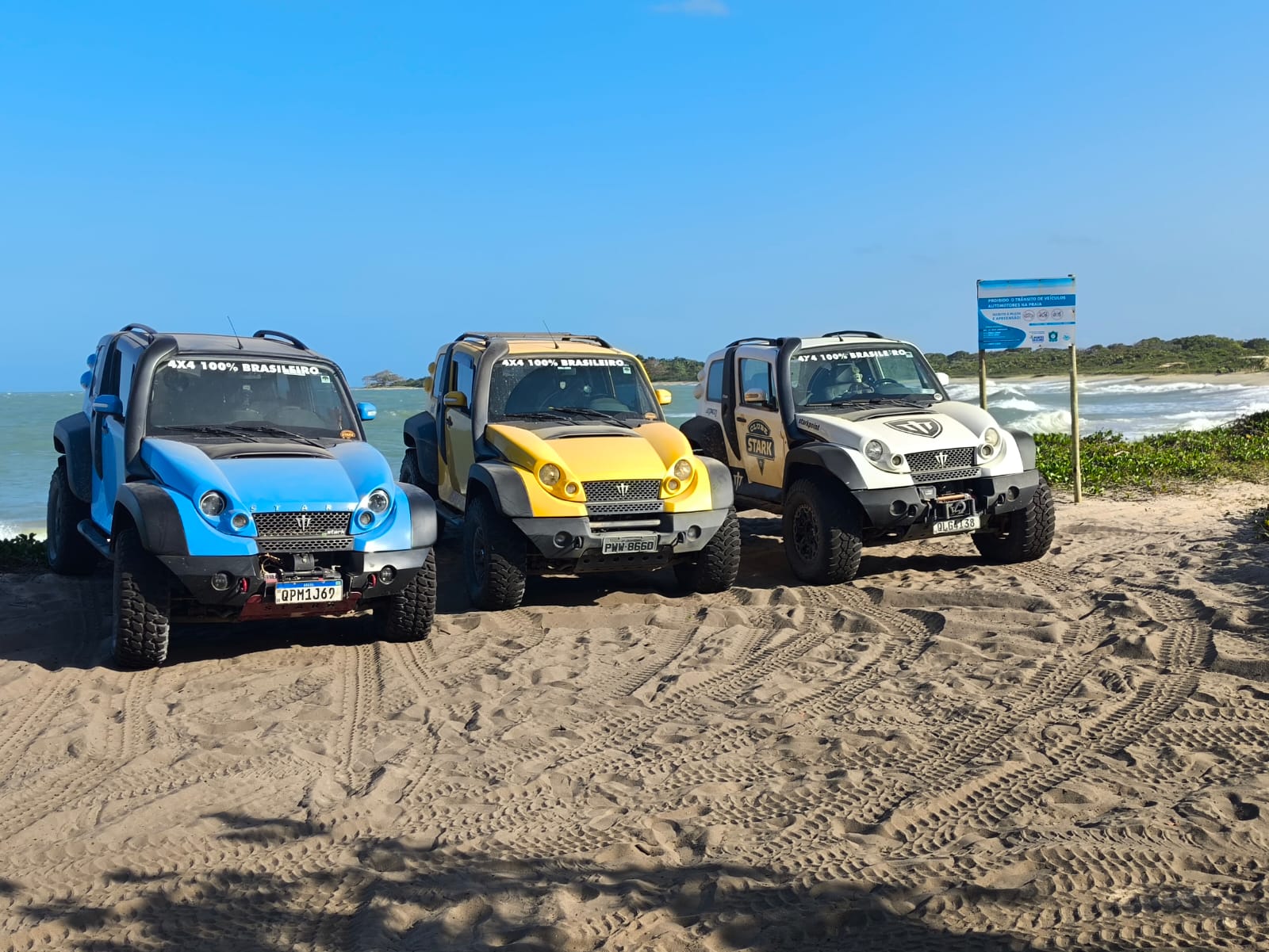 Três jipes 4x4 na areia, de frente para o mar